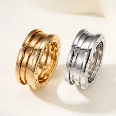 Stacked gold and silver rings with spiral band design on a plain background