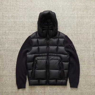 Black hooded puffer jacket with quilted body and knitted sleeves on a hanger